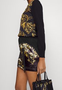 Svart långärmad topp med gyllene utsmyckning, i kombination med en svart och gyllene mönstrad minikjol och en liten svart handväska med gulddetaljer.