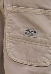 Μπεζ υφασμάτινη τσέπη με ραμμένα άκρα και μικρή ραμμένη ετικέτα με την επιγραφή «JACK & JONES COTTON DRY GOODS DIV. ESTABLISHED 1990.»