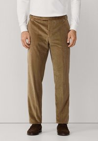 Bruine corduroy broek met verticale ribbels en een getailleerde pasvorm, voorzien van een platte voorkant en zijzakken, aangevuld met bruine schoenen.