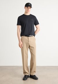 Tricou negru din bumbac cu un logo texturat, pantaloni khaki cu croi drept și adidași negri. Design simplu, fără modele sau accente.