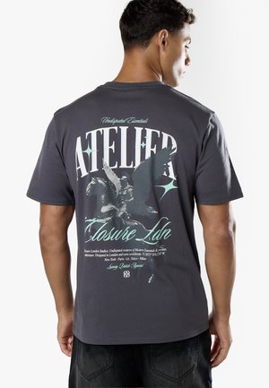 Mann, der von hinten gesehen wird, trägt ein dunkelgraues T-Shirt mit großem weißem und türkisfarbenem Text und einer Grafik eines geflügelten Pferdes mit Reiter auf dem Rücken.