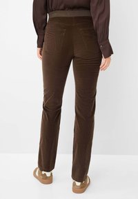 Bruine corduroy broeken met een slim fit, voorzien van een gestructureerd oppervlak, twee achterzakken en een elastische tailleband. G gedragen met tan kleurige schoenen.