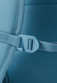 Μπλε υφασμάτινος ιμάντας με πλαστικό κούμπωμα, με υφή στην ύφανση. Το κούμπωμα είναι γκρι, με ετικέτα που περιέχει λογότυπο, προσφέροντας ασφαλή κλείσιμο.