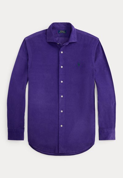 Μωβ πουκάμισο από κοτλέ με κουμπιά, αιχμηρό γιακά και μακριά μανίκια. Διαθέτει πράσινο κεντημένο λογότυπο και ασημένια κουμπιά κατά μήκος του μπροστινού μέρους.