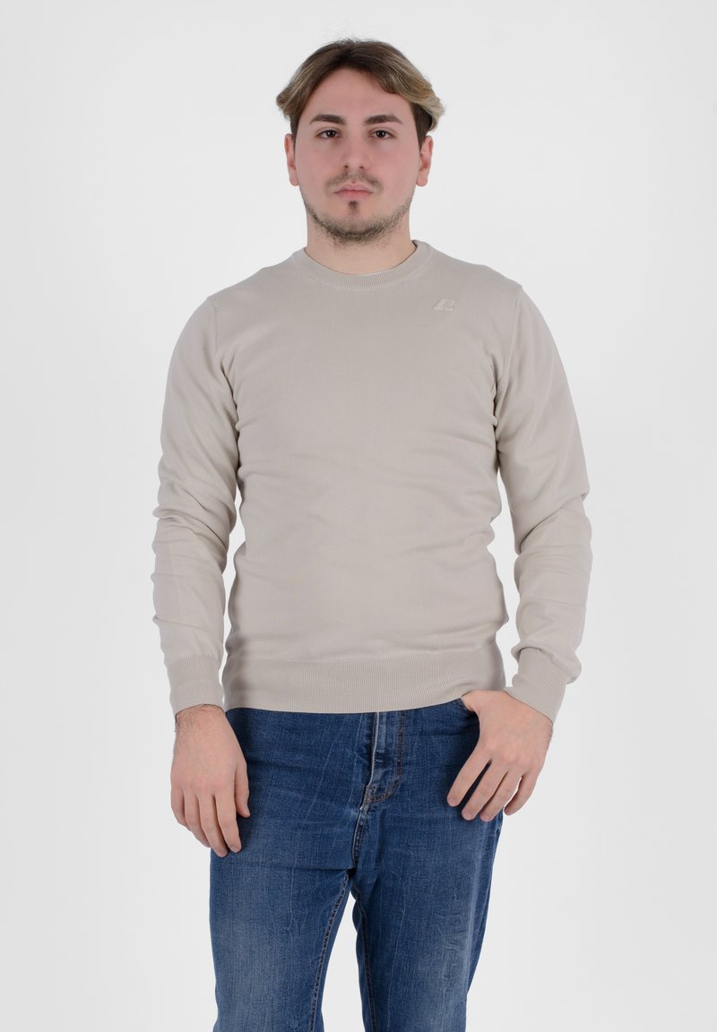 Maglione beige a maniche lunghe con colletto e polsini a coste, abbinato a jeans in denim blu. Design semplice, texture morbida e branding minimal.