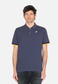 Polo shirt blu navy con colletto, due bottoni e strisce gialle e nere in contrasto sulle maniche. Presenta un piccolo logo sul petto.
