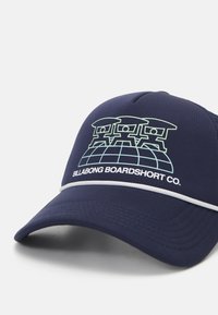 Marinehatt laget av stoff med en strukturerte form, med et lysegrønt grafikk og teksten "Billabong Boardshort Co." over fronten.