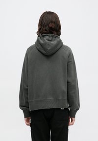 Sudadera gris oscuro de corte relajado, con capucha ajustable y puños acanalados. Diseño minimalista sin patrones ni acentos visibles.