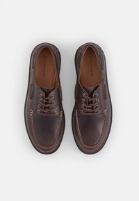 Dark brown leather shoes with beige stitching, round toe, and two pairs of eyelets. Smooth texture and subtle design details on the upper.