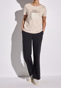 Camiseta de algodón beige con mangas cortas y un diseño gráfico. Pantalones de pierna ancha negros, hechos de una tela suave, combinados con zapatillas blancas.