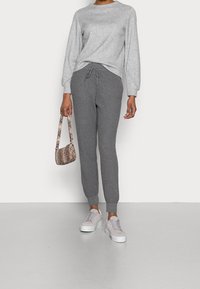 Grijze, gestructureerde trui met een ribbelontwerp, gecombineerd met bijpassende grijze ribbel joggers met een elastische tailleband en trekkoord. Witte sneakers en een tas met slangenprint.