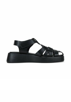 Sandalias de cuero negro con diseño superior trenzado, correa trasera y suela de plataforma gruesa para mayor altura y comodidad.