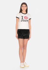 T-shirt bianca con bordo nero e grafica di labbra rosse, abbinata a una gonna nera in velluto con volant e sneakers bianche. Un look casual e vivace.