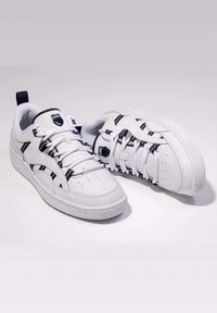 White athletic shoes with a smooth leather finish, featuring black accents, a rounded toe, and a textured rubber sole. Laces and logo detail visible.