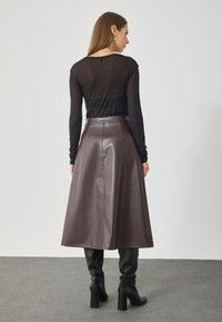 Falda midi de cuero sintético marrón con diseño acampanado, textura suave y detalles de costura en la parte trasera, combinada con una blusa ajustada de manga larga negra.