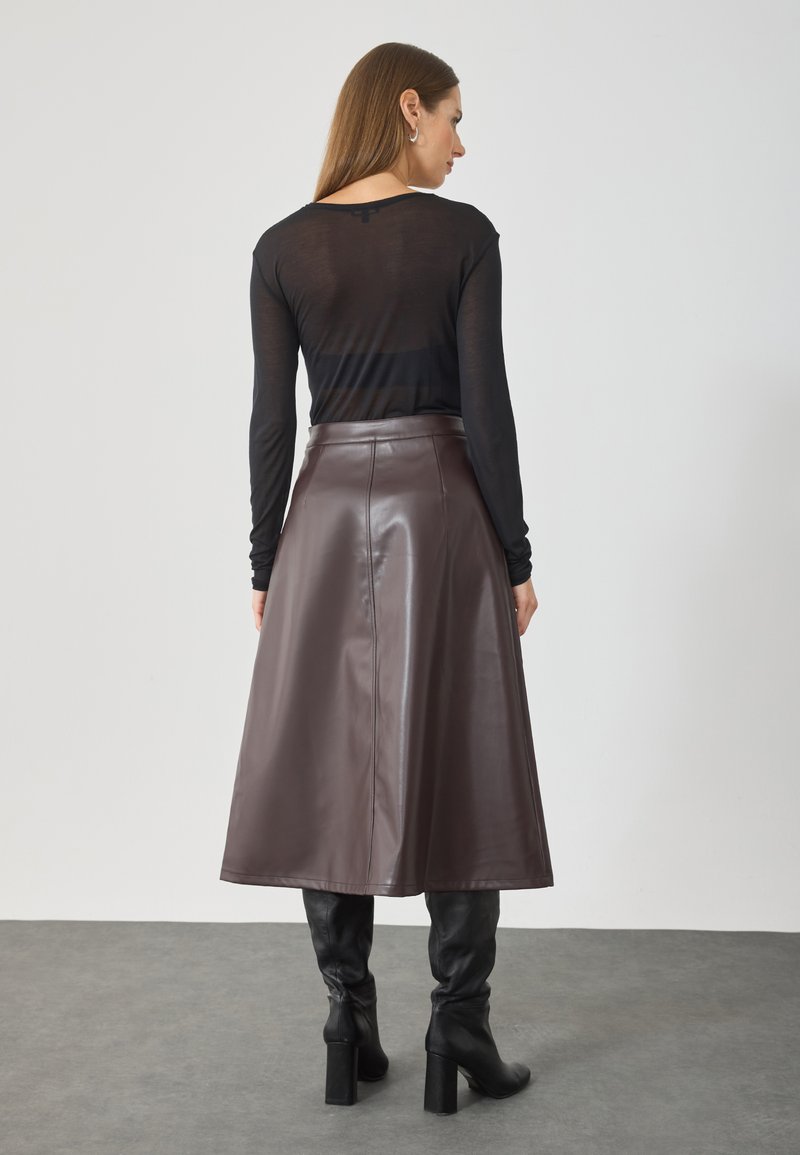 Falda midi de cuero sintético marrón con diseño acampanado, textura suave y detalles de costura en la parte trasera, combinada con una blusa ajustada de manga larga negra.