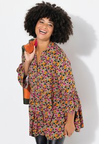 Bloementunic met een V-hals, voorzien van oranje, roze en groene patronen. Lange mouwen met ruffles, gecombineerd met zwarte legging.