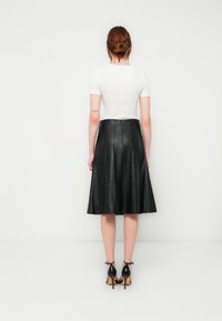 Black leather A-line skirt with vertical pleats, paired with a white short-sleeve top and black high-heeled sandals. Back view presented.