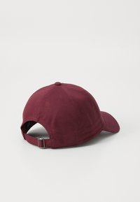 Bordeaux baseball cap med buet skygge, knap på toppen og en justerbar rem bagpå med metallic hardware accent.