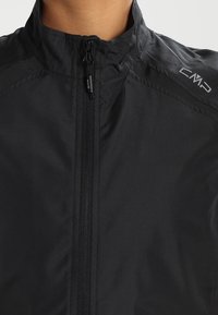 Czarna kurtka z gładkiego, lekkiego materiału, z wysokim kołnierzem, pełnym zamkiem z przodu i logotypem CMP na ramieniu.