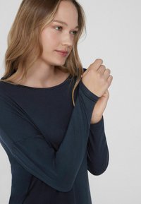 Langärmliges, marineblaues Oberteil mit rundem Ausschnitt, aus weichem Stoff und eng anliegenden Ärmeln. Detail der Hand am Ärmelende ist sichtbar.