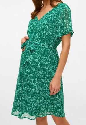 Zielona sukienka w groszki wykonana z lekkiego materiału. Dekolt w serek, krótkie falbankowe rękawy oraz pas wiązany w talii. Rozkloszowany dół.