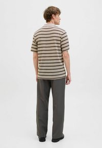 Polo cu dungi în tonuri de bej și maro, cu mâneci scurte și tiv drept. Asortat cu pantaloni larghi gri și încălțăminte neagră.