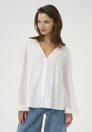 Hvid bluse med V-hals, fuld længde, teksturerede gennemsigtige ærmer og knaplukning foran. Båret med denimbukser.