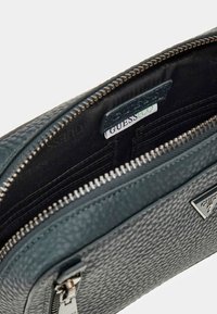 Borsa a tracolla in pelle texturizzata verde scuro con chiusura a zip, scomparti interni per carte e etichetta con marchio. Presenta una cerniera e dettagli hardware in tono argento.