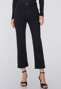 Pantalones de mezclilla negros con cintura alta, diseño de pierna ancha y corta, cinco bolsillos y cierre frontal con botón. El material parece suave y resistente.