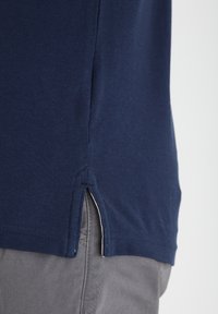 Marineblå skjorte med korte ermer og teksturert overflate, med sidespalter nær kanten og klassisk snitt. Stoffet ser lett og pustende ut.