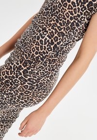 Top s krátkým rukávem v leopardím vzoru, přiléhavý střih s nařasením, vyrobený z měkké elastické tkaniny v hnědých a černých odstínech.