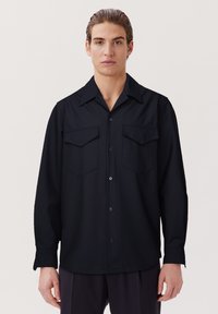 Schwarzes Langarmhemd mit Knopfverschluss, spitzem Kragen und zwei Brusttaschen. Glatte Textur und lockere Passform.