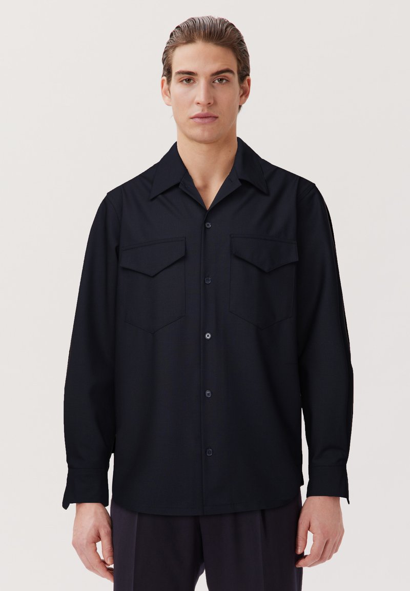 Schwarzes Langarmhemd mit Knopfverschluss, spitzem Kragen und zwei Brusttaschen. Glatte Textur und lockere Passform.