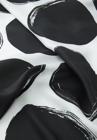 Black and white patterned fabric featuring large circular shapes with brushstroke accents, smooth texture, and flowing drape.