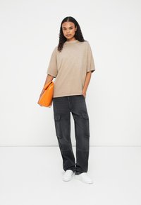 Beige oversized t-shirt lavet af blødt stof, parret med mørkegrå cargo-bukser med flere lommer. Orange clutch og hvide sneakers.