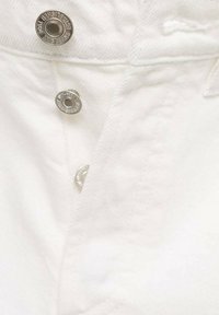 Tissu en denim blanc avec des boutons métalliques argentés et des coutures détaillées, avec une ouverture de poche visible et une texture lisse.