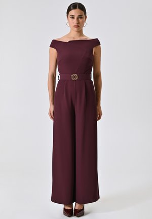 Burgunderfarbener Jumpsuit mit schulterfreiem Design, weitem Bein und taillierter Passform, verziert mit einer dekorativen goldfarbenen Schnalle. Glatte Textur.