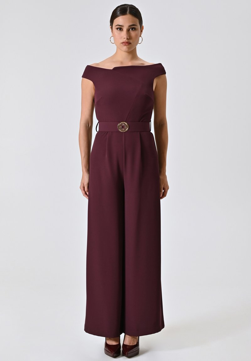 Burgunderfarbener Jumpsuit mit schulterfreiem Design, weitem Bein und taillierter Passform, verziert mit einer dekorativen goldfarbenen Schnalle. Glatte Textur.
