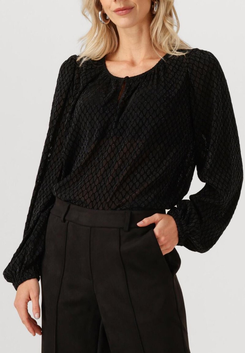 Zwarte blouse met een gestructureerd, diamantpatroon, luchtige mouwen en een sleutelgatdecolleté, gecombineerd met hoge zwarte broek.