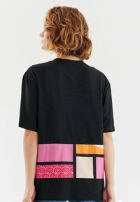 Černé tričko s krátkým rukávem, které na zadní straně zdobí vícebarevný geometrický design s růžovými, oranžovými a vzorovanými akcenty.