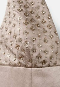 Tejido con cuentas que presenta una textura similar a la seda en color beige, adornado con patrones florales en hilos dorados y plateados, con pequeñas cuentas como acentos.