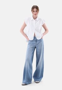 Weißes Kurzarmhemd mit Knopfleiste, kombiniert mit hellblauen, weit geschnittenen Jeans, die eine weiche Denim-Textur und eine lässige Silhouette präsentieren.