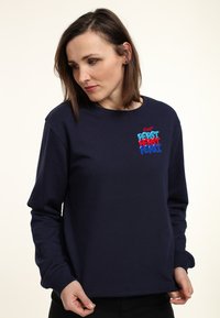 Felpa blu navy in cotone con maniche lunghe, scollatura rotonda e un design grafico colorato che presenta la scritta "Pepsi" in caratteri in grassetto.