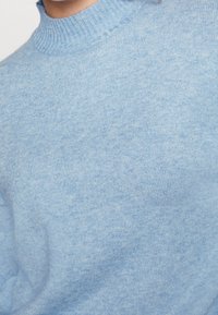 Pull bleu clair tricoté avec un col cheminée côtelé, visible du cou jusqu'au milieu du torse.