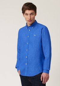 Camisa azul de manga larga en una tela ligera y texturizada. Cuenta con un cuello, botones blancos y un pequeño logo bordado.