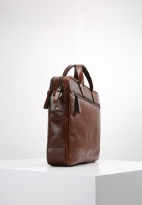 Attaché-case en cuir marron avec une finition texturée, deux poignées supérieures et une ouverture zippée. Présente des accessoires en ton doré et des poches latérales.