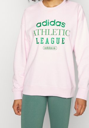 Person iført pink Adidas sweatshirt med grøn "ATHLETIC LEAGUE" tekst og grønne sportbukser med hvide striber i siderne.