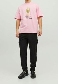 T-shirt en coton rose avec un graphique de cactus vert et un texte noir, associé à un pantalon cargo noir et des chaussures noires.