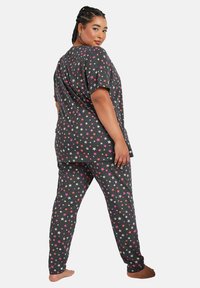 Conjunto de pijama gris con mangas cortas y corte holgado, que presenta un patrón de estrellas en rosa y blanco tanto en la parte superior como en los pantalones. Textura de tela suave.